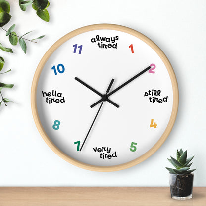 Hanging wall clock with a swedish minimal design. On 4 quadrants, there are variations of "tired" instead of the hour markers. The remaining numbers are cheerful bright colors. This clock has a wooden frame.