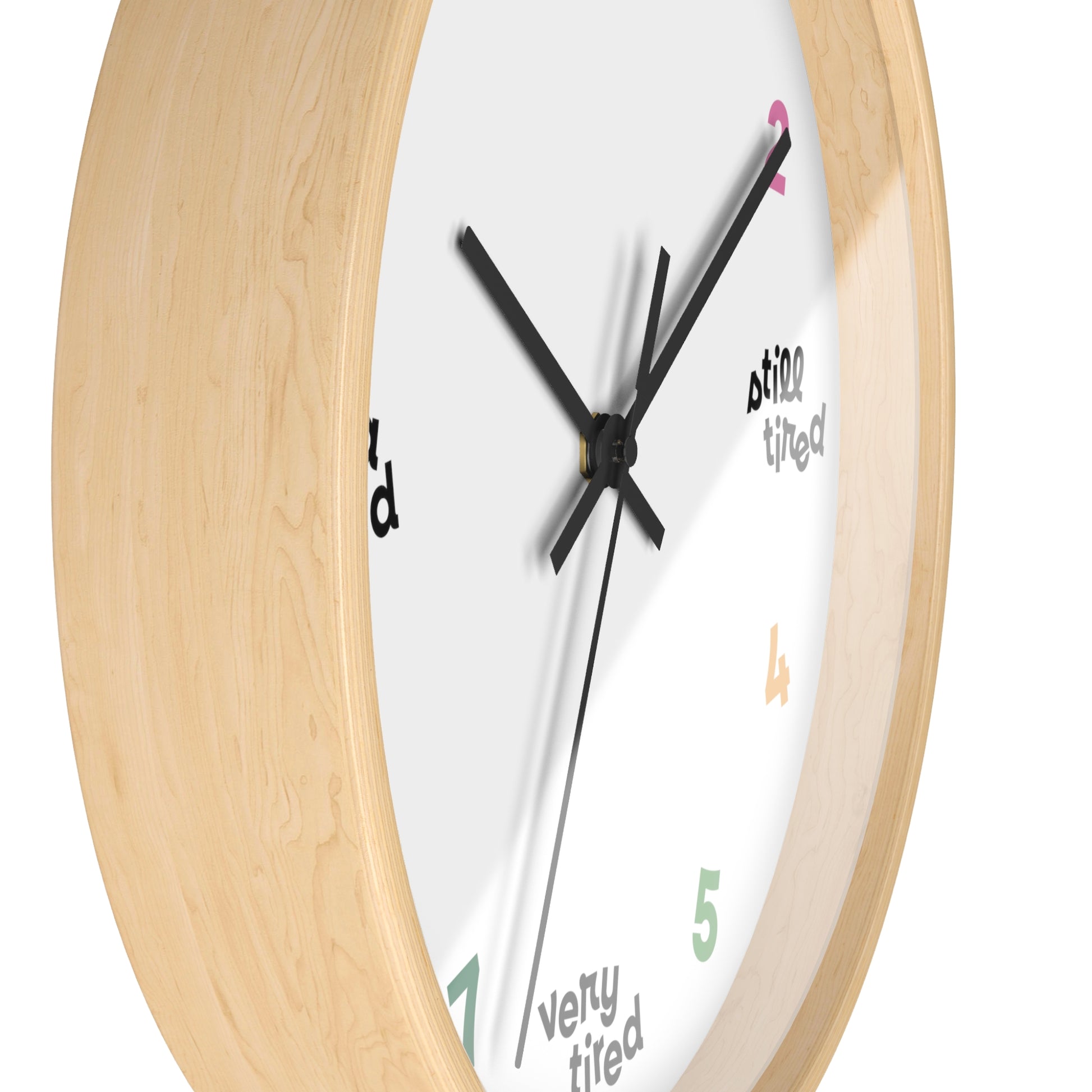 Hanging wall clock with a swedish minimal design. On 4 quadrants, there are variations of "tired" instead of the hour markers. The remaining numbers are cheerful bright colors. This clock has a wooden frame. Side view shown.