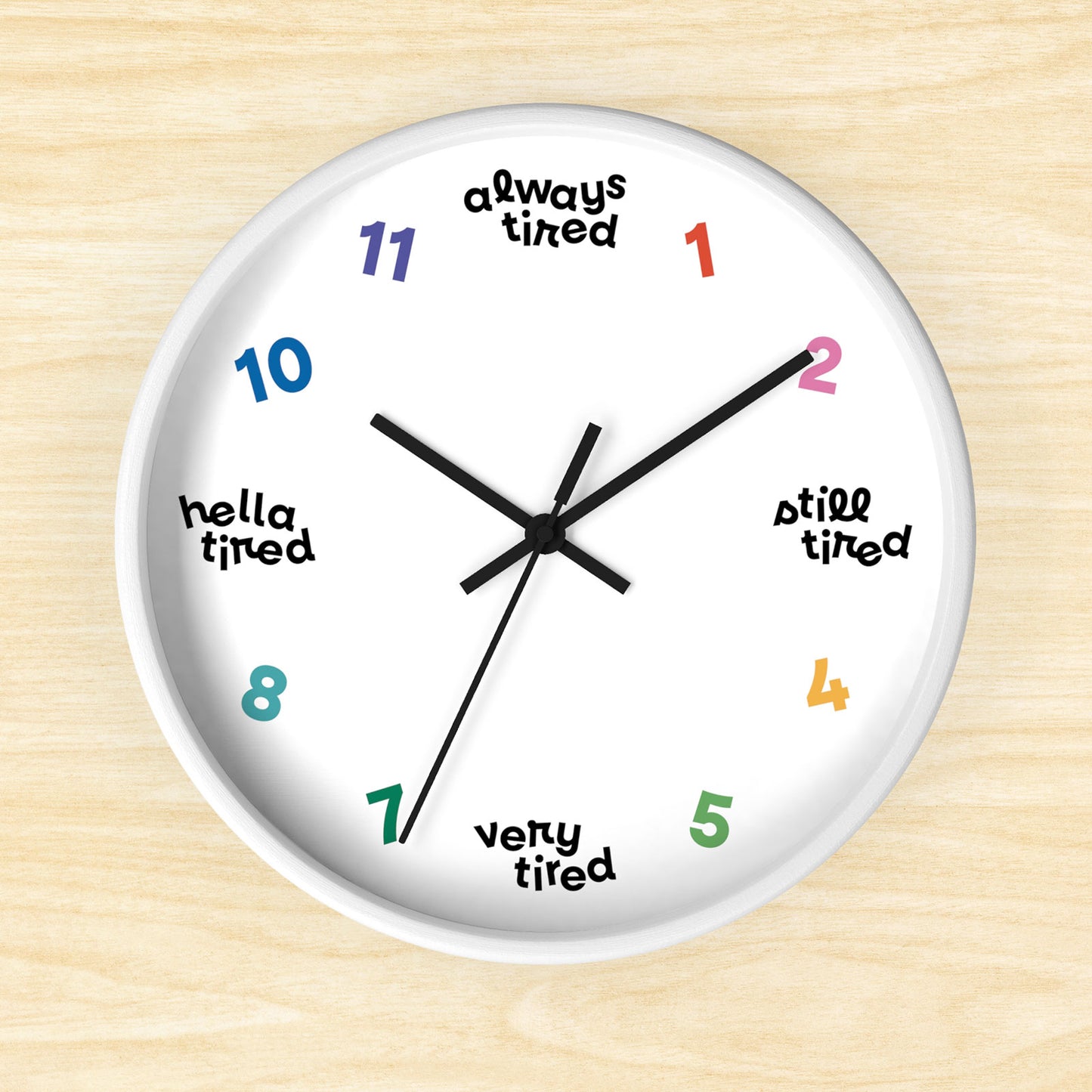 Hanging wall clock with a swedish minimal design. On 4 quadrants, there are variations of "tired" instead of the hour markers. The remaining numbers are cheerful bright colors. This clock has a white frame.
